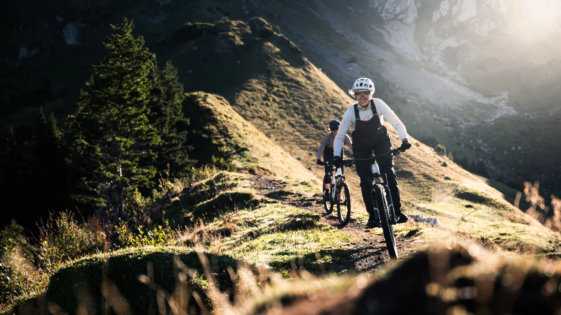 Mountainbikerin springt mit ihrem Trail Bike über eine Alpwiese vor markanter Felswand