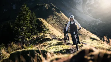 Mountainbikerin springt mit ihrem Trail Bike über eine Alpwiese vor markanter Felswand