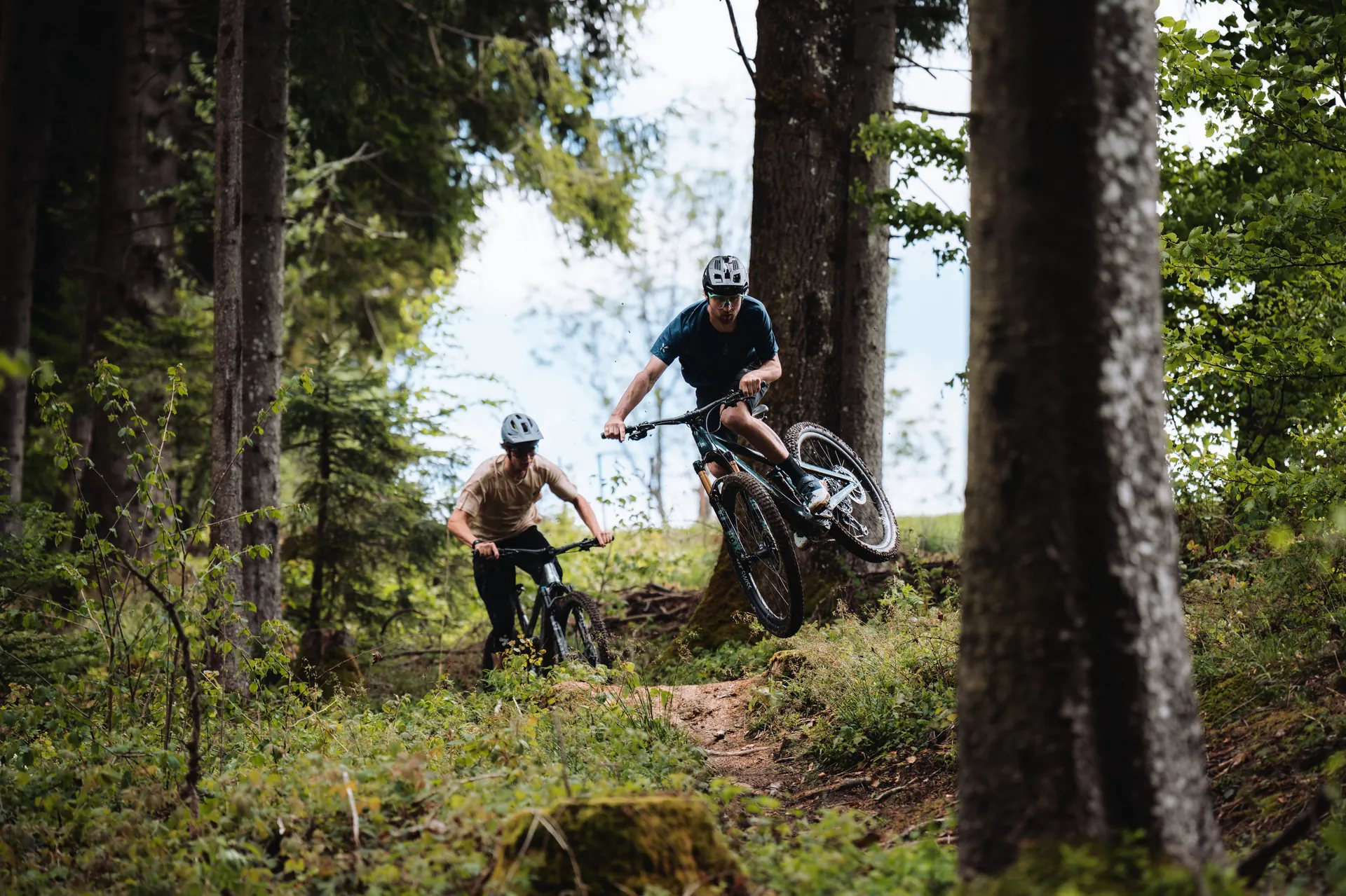 E-Mountainbiker springt über einen Trail-Absatz im Wald