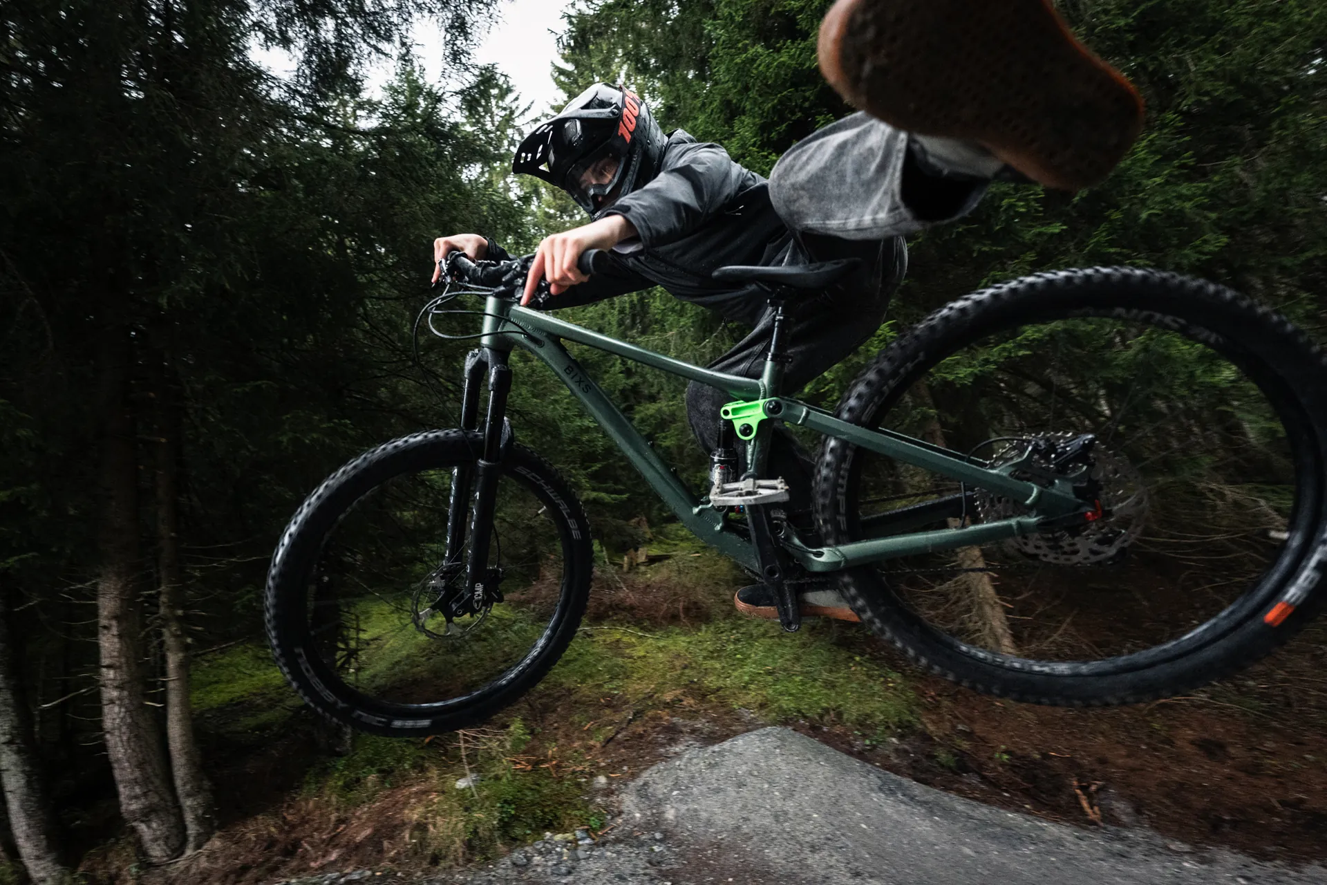 Fahrer mit Vollvisierhelm im Sprung über Trail-Kicker im Wald