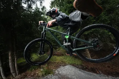 Fahrer mit Vollvisierhelm im Sprung über Trail-Kicker im Wald