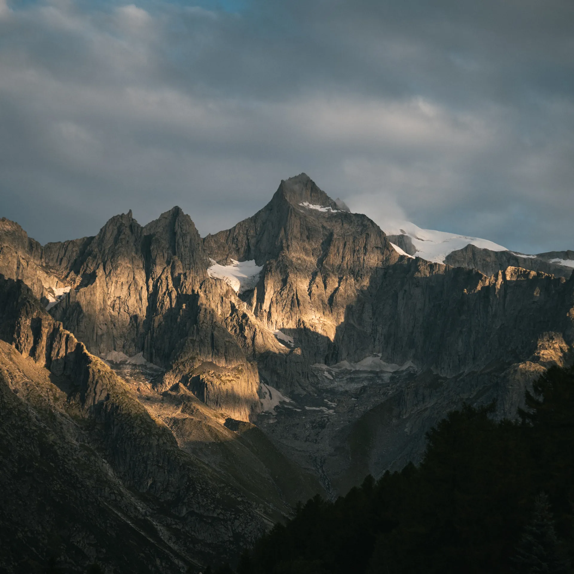Schroffe Alpengipfel mit Schneefeldern im Abendlicht unter bewölktem Himmel