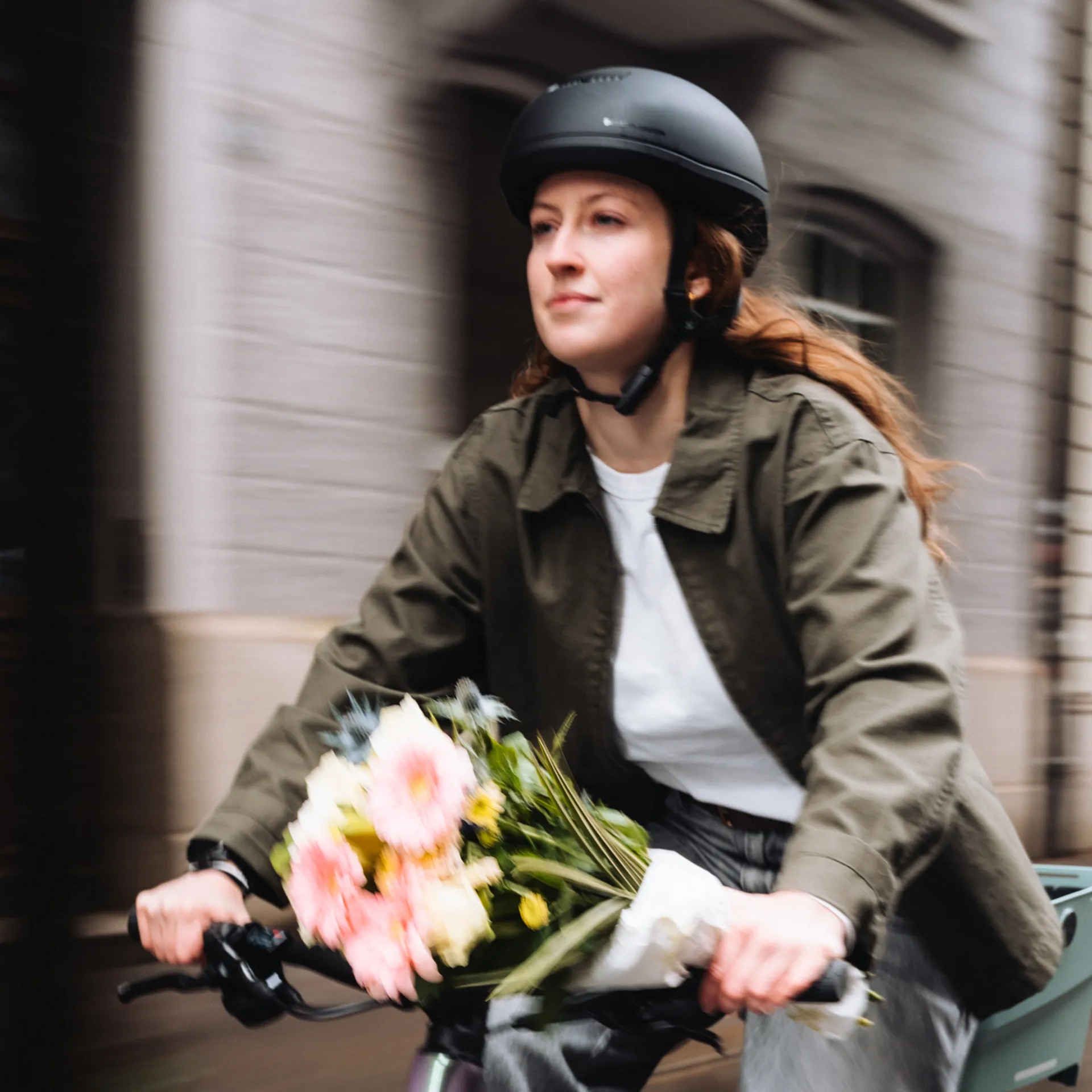 Fahrerin mit Helm transportiert einen Blumenstrauss auf ihrem Urban Bike durch die Stadt