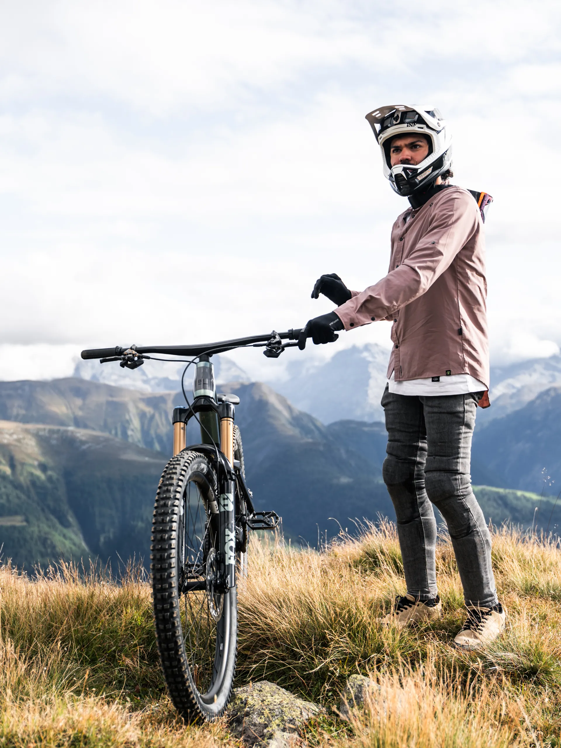 Fahrer mit Fullface-Helm steht neben seinem BIXS Lane auf einer Alpwiese mit Bergpanorama