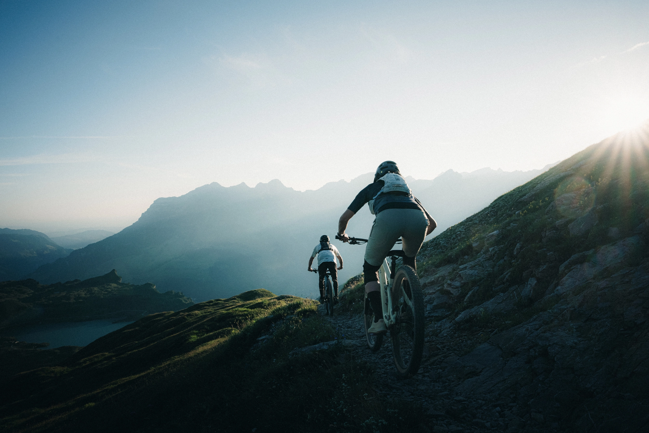 Zwei Enduro-Fahrer fahren im Gegenlicht einen alpinen Bergpfad hinunter