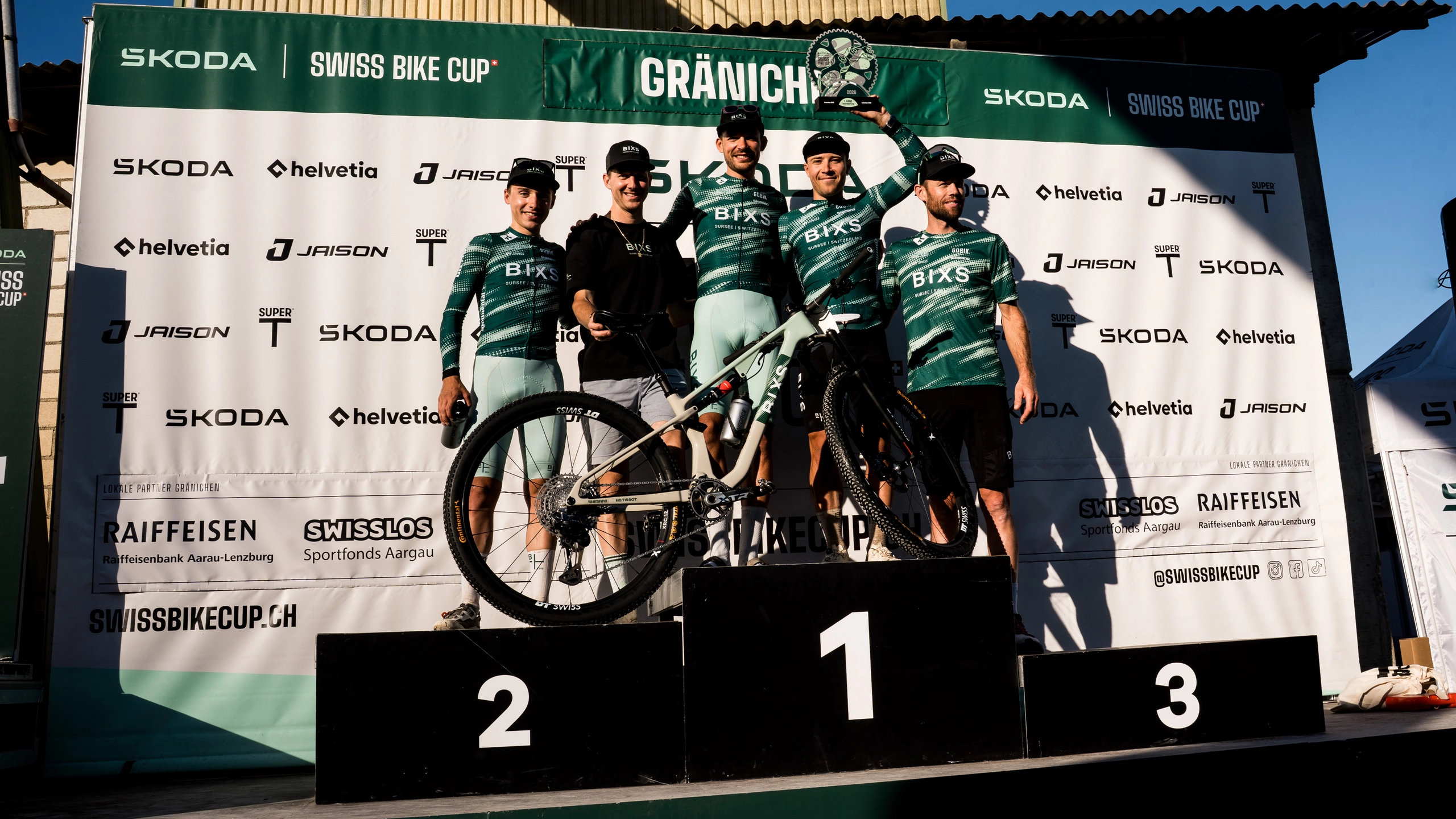 Fünf Personen des BIXS-Teams stehen mit einem Race-Bike auf dem Podest vor der Swiss-Bike-Cup-Wand in Gränichen