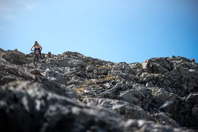 Einzelner Enduro-Biker fährt über schroffen Felsgrat vor klarem blauem Himmel, viel freier Bildraum oben