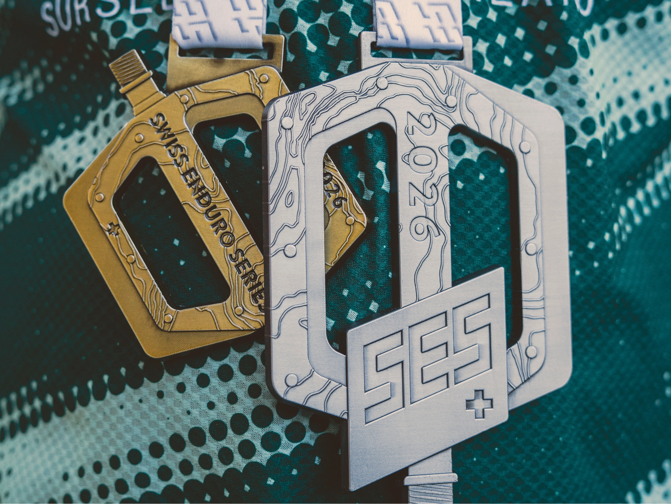 Zwei Medaillen der Swiss Enduro Series 2026 in Pedalform, Gold und Silber, auf einem grünen BIXS-Trikot