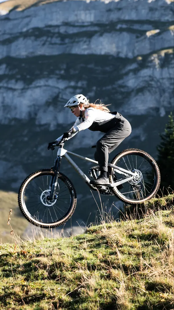 Mountainbikerin springt mit ihrem Trail Bike vor Felswand in den Bergen