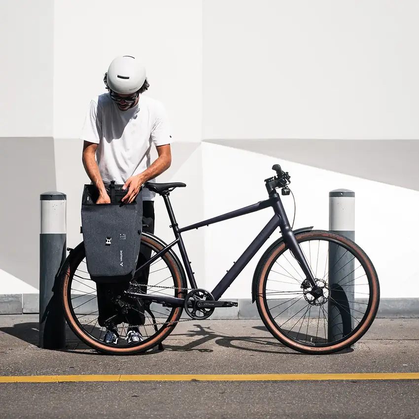 Mann befestigt Gepäcktasche an BIXS E-Urban-Bike vor minimalistischer Fassade