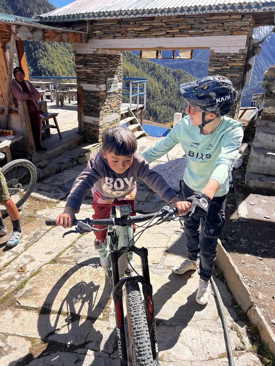 Fahrer zeigt einem Kind das Bike vor einer Bergsteinlodge im Himalaya