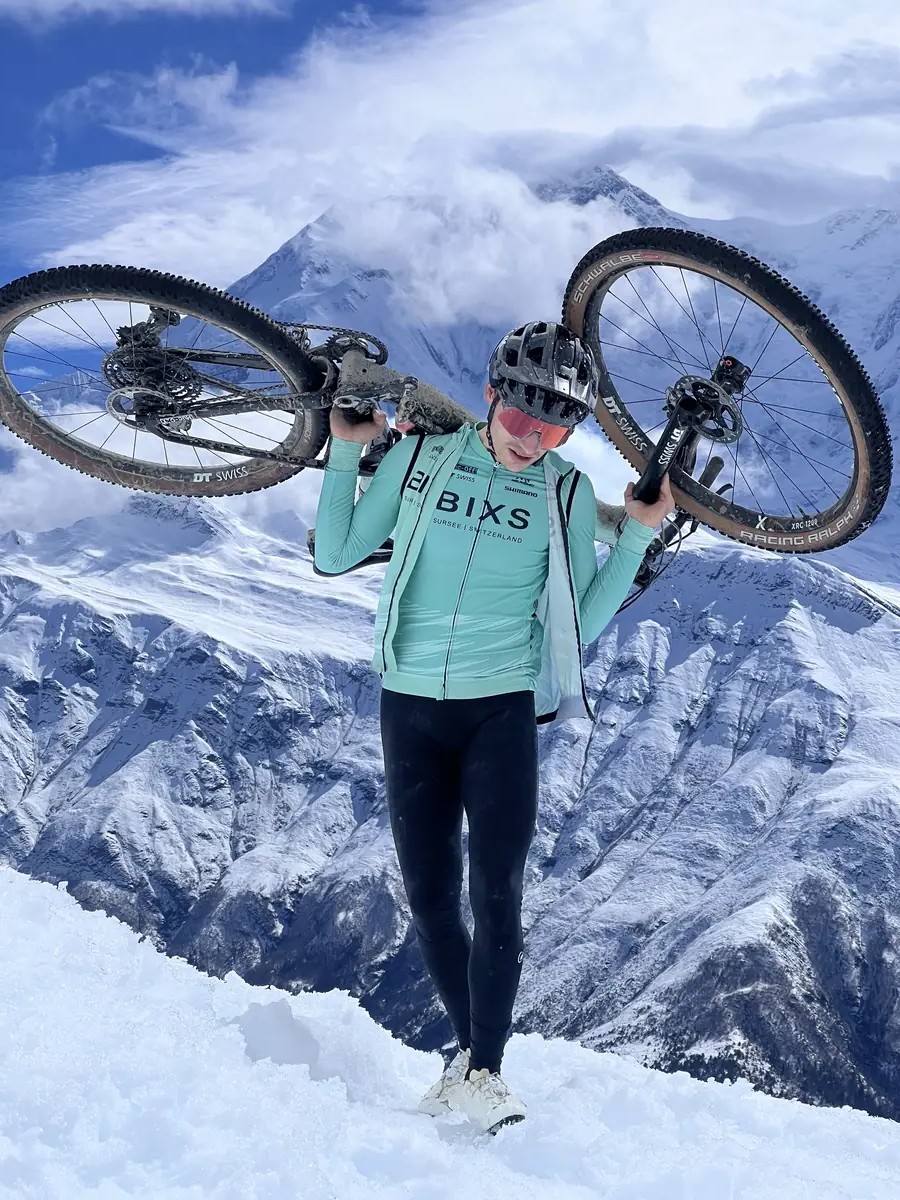 Fahrer trägt Bike über der Schulter durch tiefen Schnee vor Berggipfeln