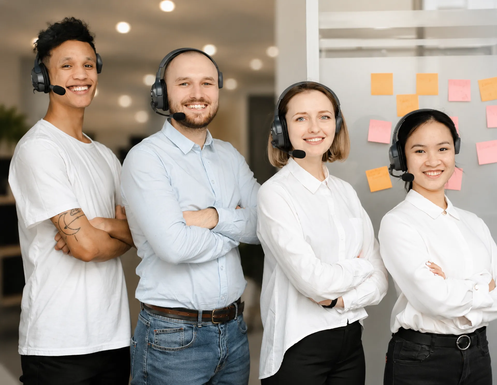 Four smiling support agents wearing headsets standing together in a contact center