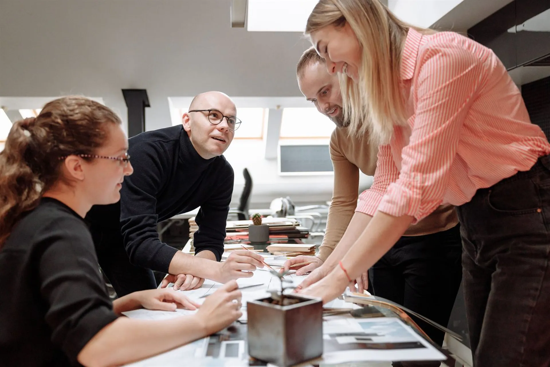 Team of four colleagues leaning over a desk covered with documents, planning together in an office