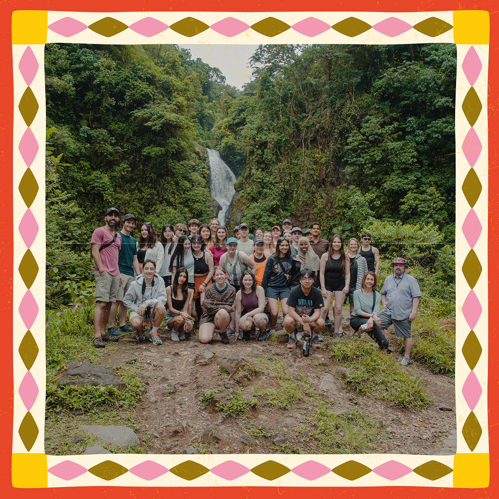 Large group of students and leaders posing on a rocky trail in lush green rainforest with a waterfall behind them in Costa Rica