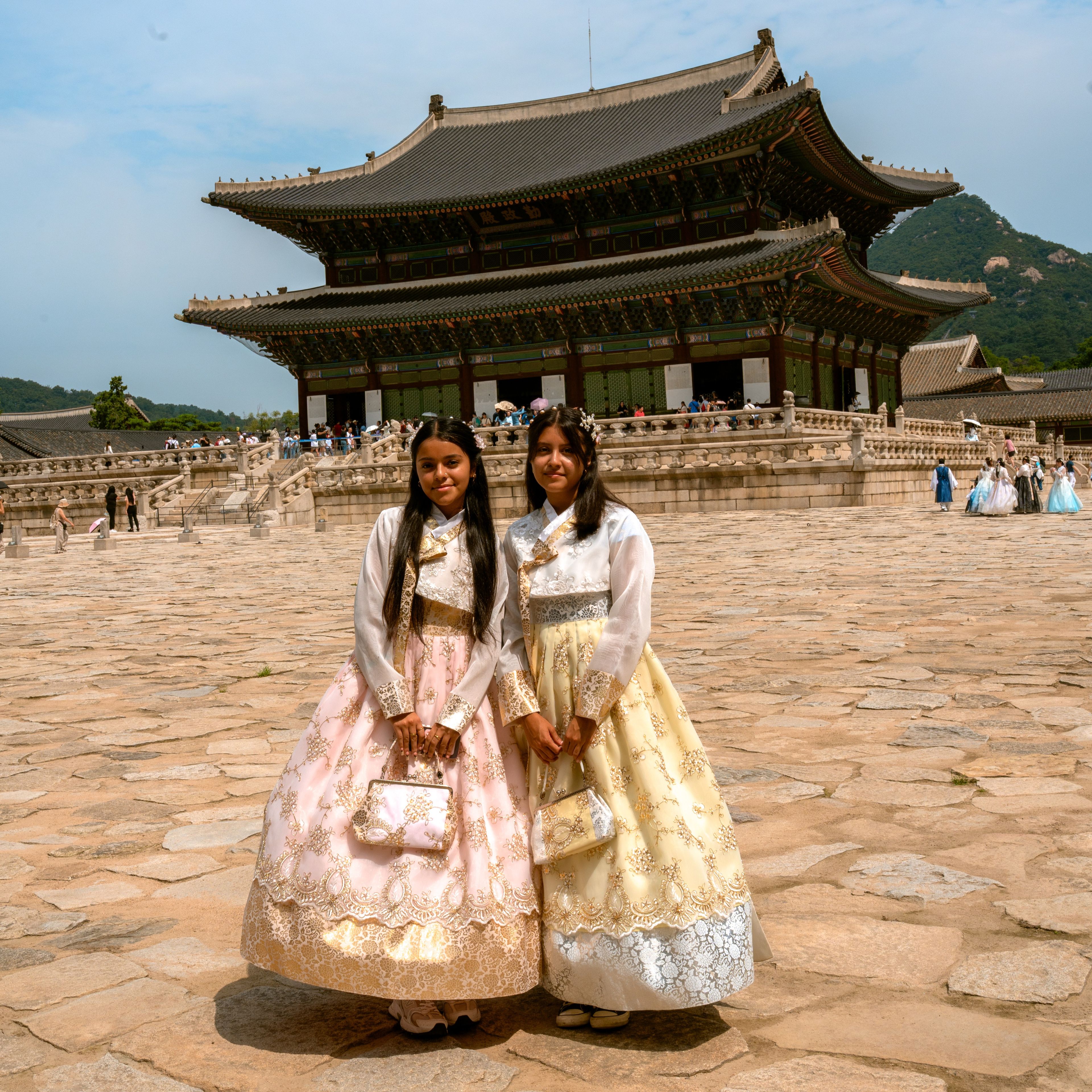 Two students in pastel traditional hanbok dresses standing in the courtyard of Gyeongbokgung Palace in Seoul, South Korea