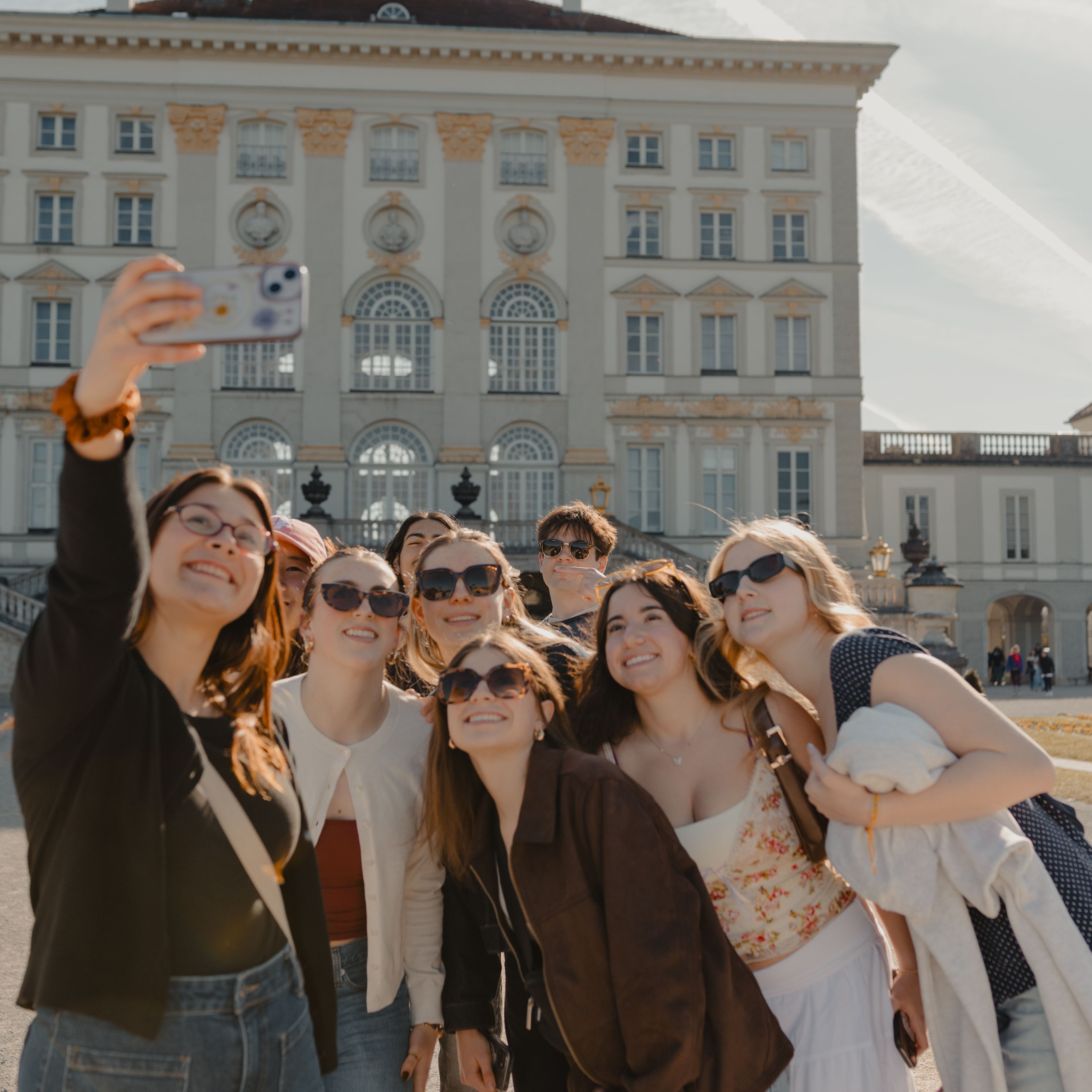 Group of smiling students taking a selfie in front of a cream-coloured neoclassical palace building in Germany