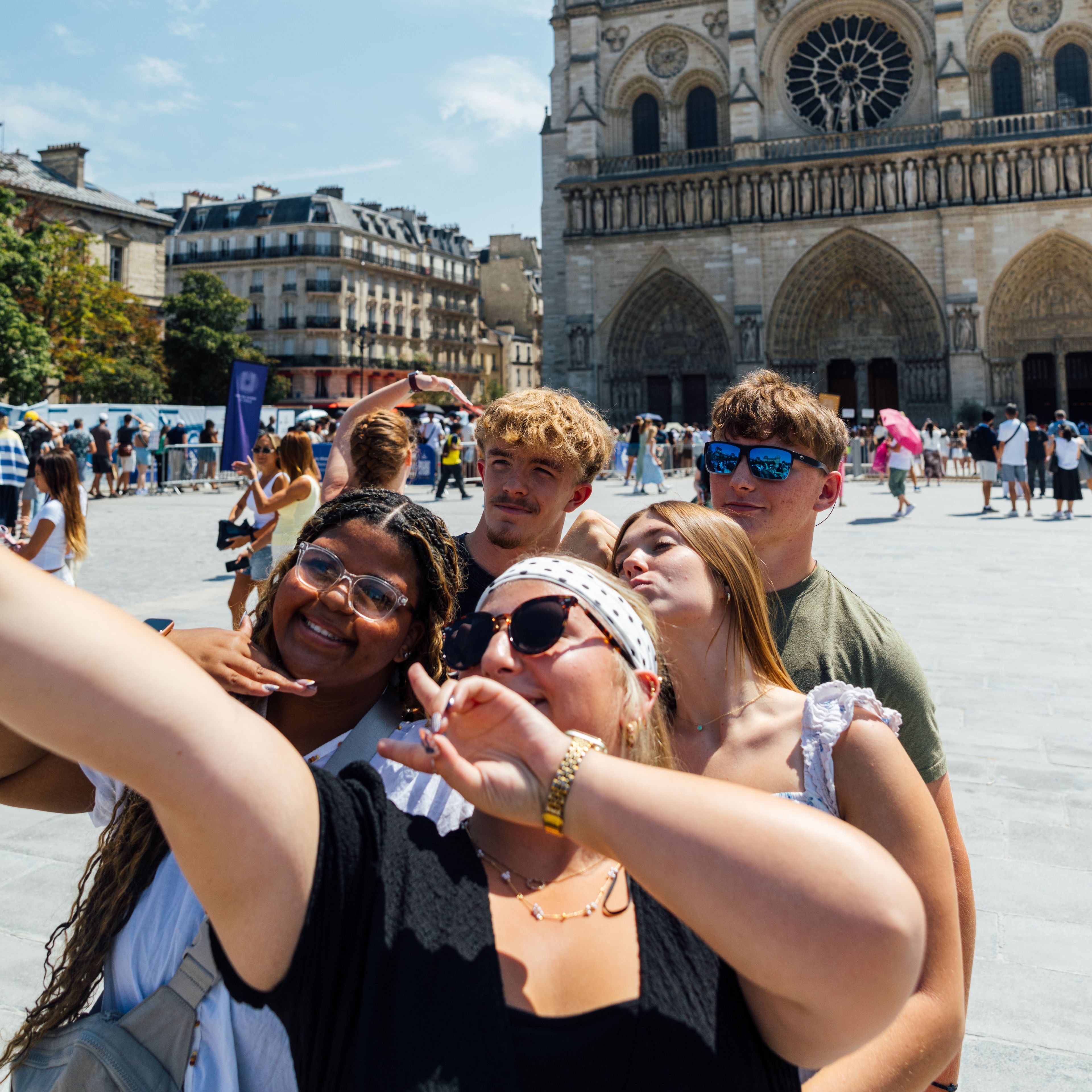 Group of smiling students taking a selfie on the plaza in front of the Gothic façade and rose window of Notre-Dame Cathedral in Paris, France