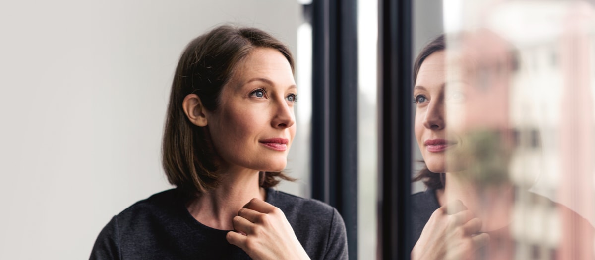 Frau steht am Fenster und schaut in die Ferne.