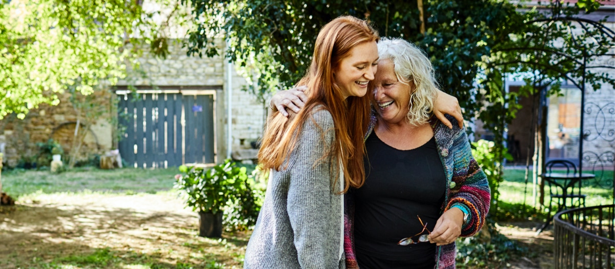 Zwei Frauen umarmen sich in einem Garten.
