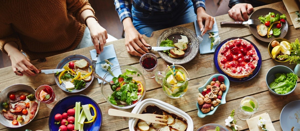 Esstisch mit gesunden Lebensmitteln an dem Menschen sitzen und essen.