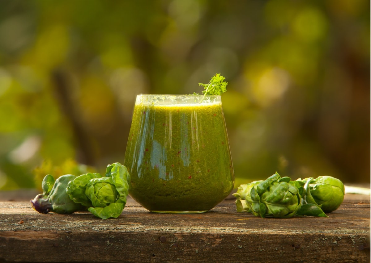 Glas mit Rosenkohl-Himbeer-Smoothie auf einem Tisch.