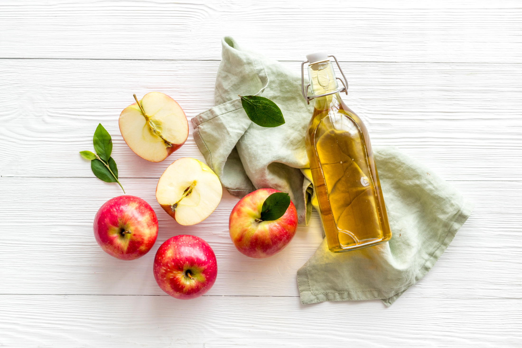 Apfel und eine Flasche mit Apfelessig auf weißem Hintergrund.