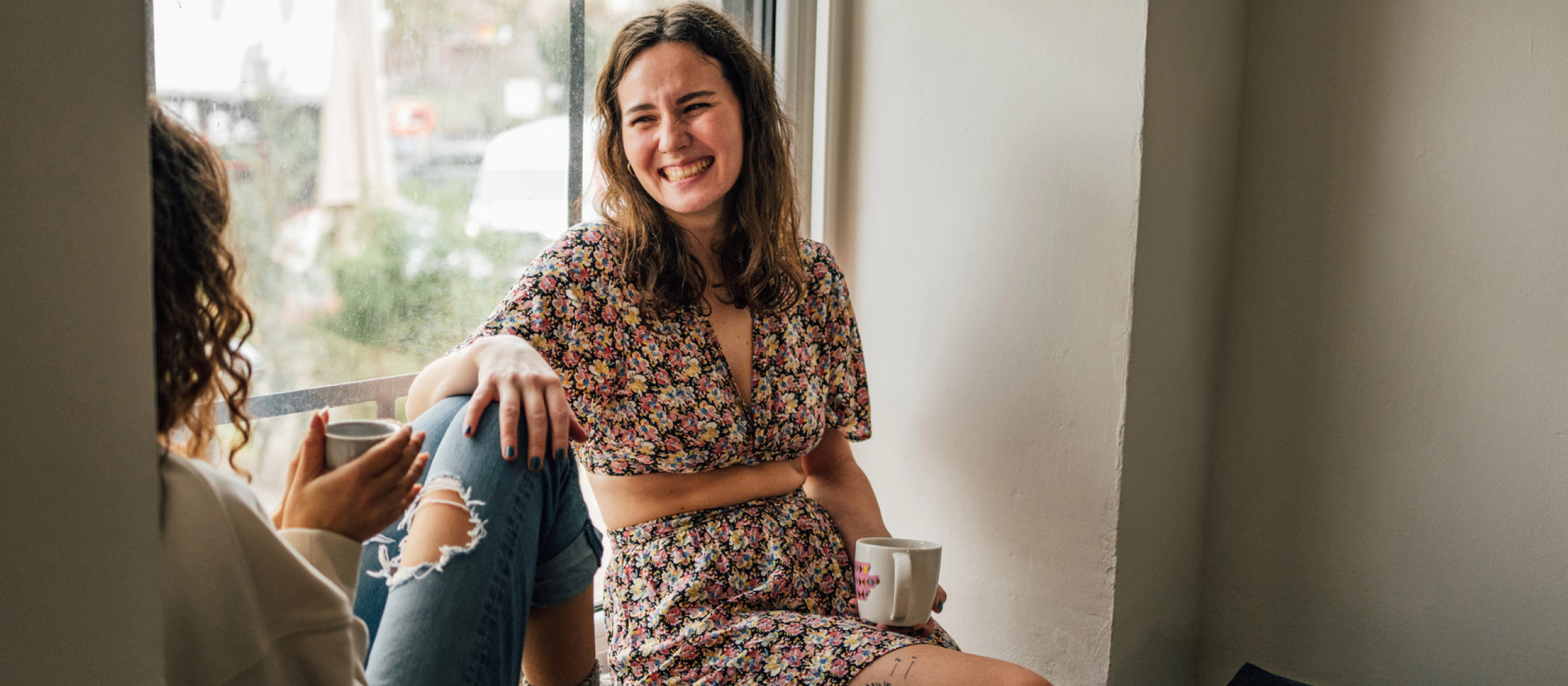 Freundinnen sitzen auf einer Fensterback und unterhalten sich.
