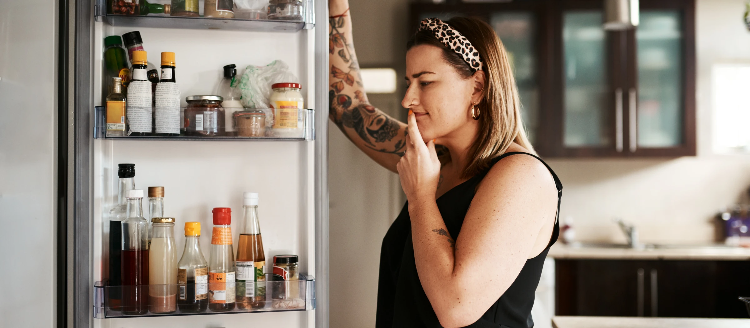 Frau steht nachdenklich vor dem Kühlschrank.