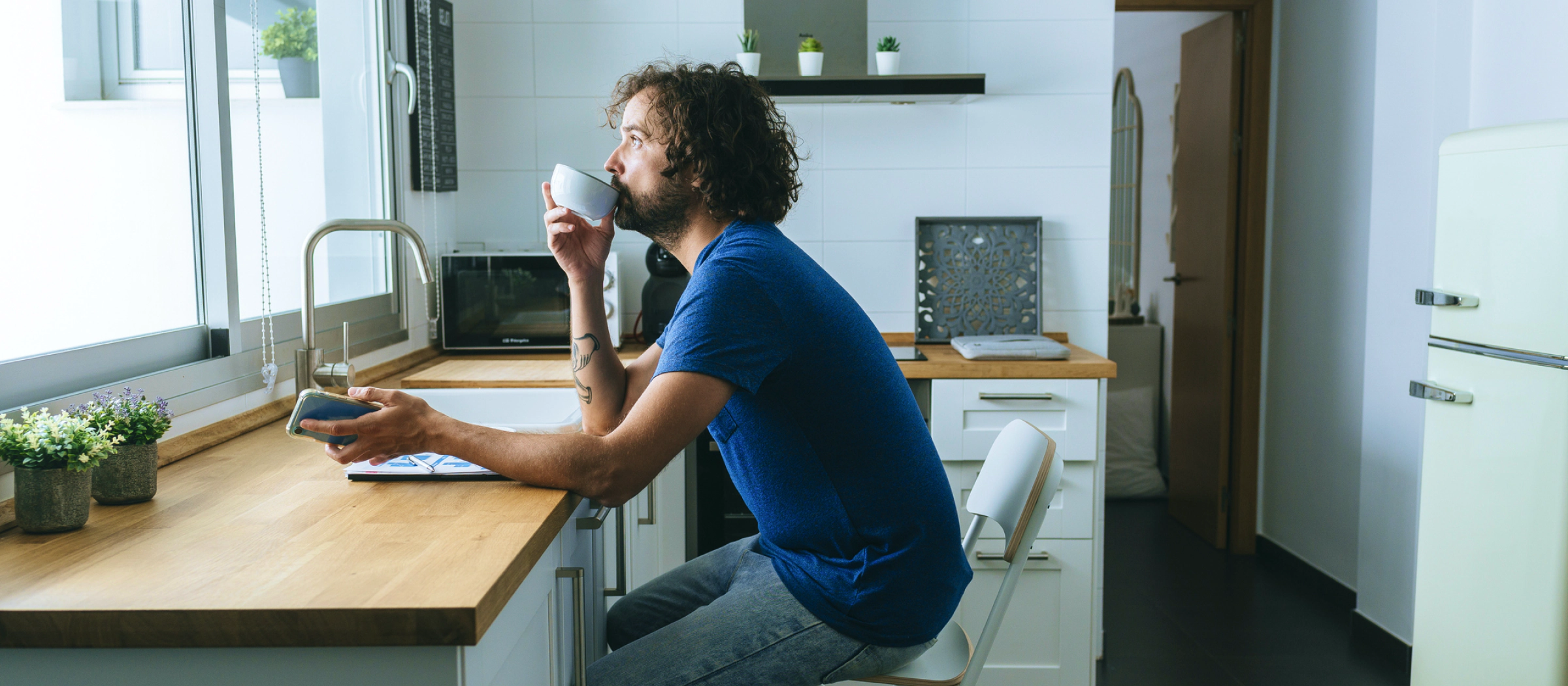 Mann sitzt in der Küche und trinkt aus einer Tasse.