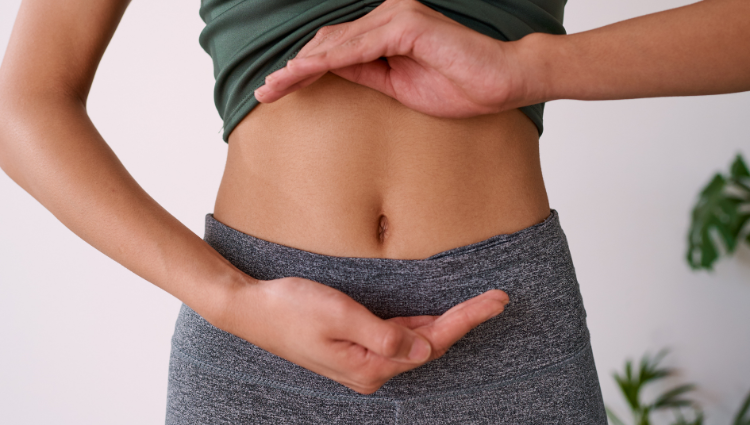 Frau in Sport bzw. Yogaklamotten hält ihre Hände vor den Bauch.