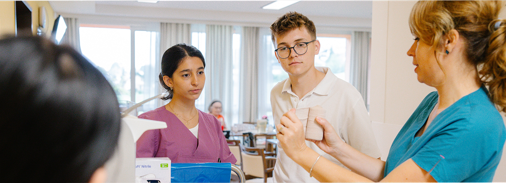 Pflegekraft erklärt zwei jungen Personen ein medizinisches Material in einem Pflegeheim.