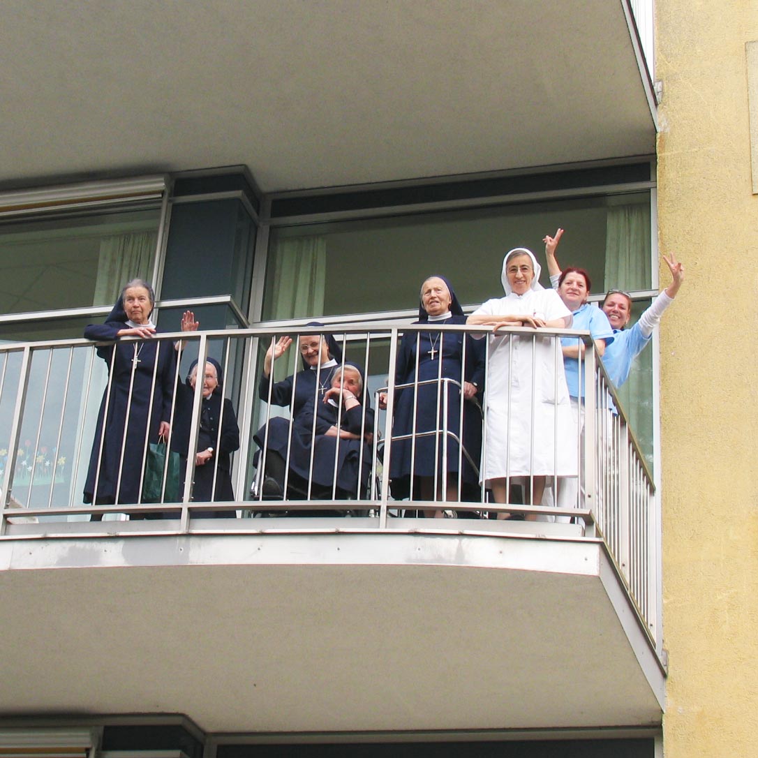 Sechs Ordensfrauen und zwei Pflegerinnen stehen am Balkon und winken