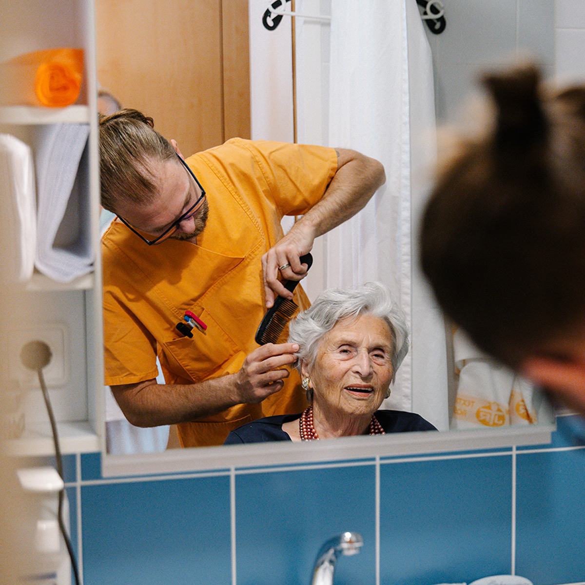 Ein Pfleger frisiert einer Bewohnerin liebevoll die Haare.