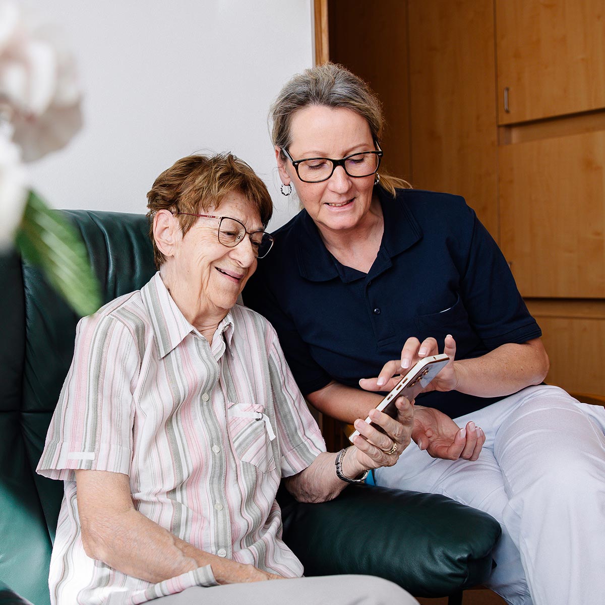 Eine Betreuerin erklärt einer älteren Dame im Betreuten Wohnen etwas am Smartphone.