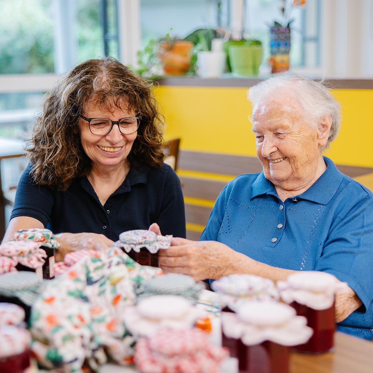 Eine ältere Dame und eine Seniorenbetreuerin verpacken selbstgemachte Marmelade.