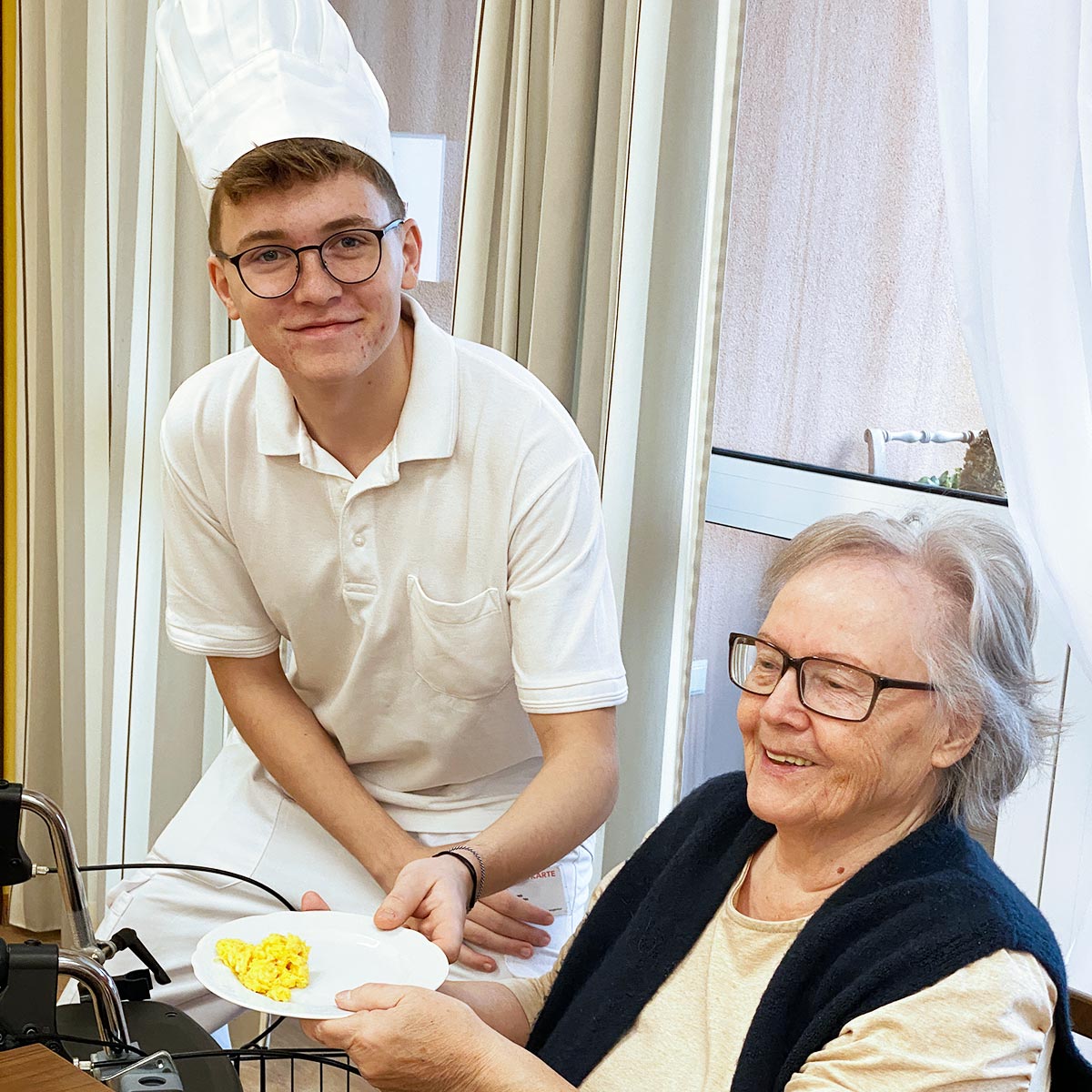 Ein Zivildiener kocht für eine Bewohnerin Eierspeis