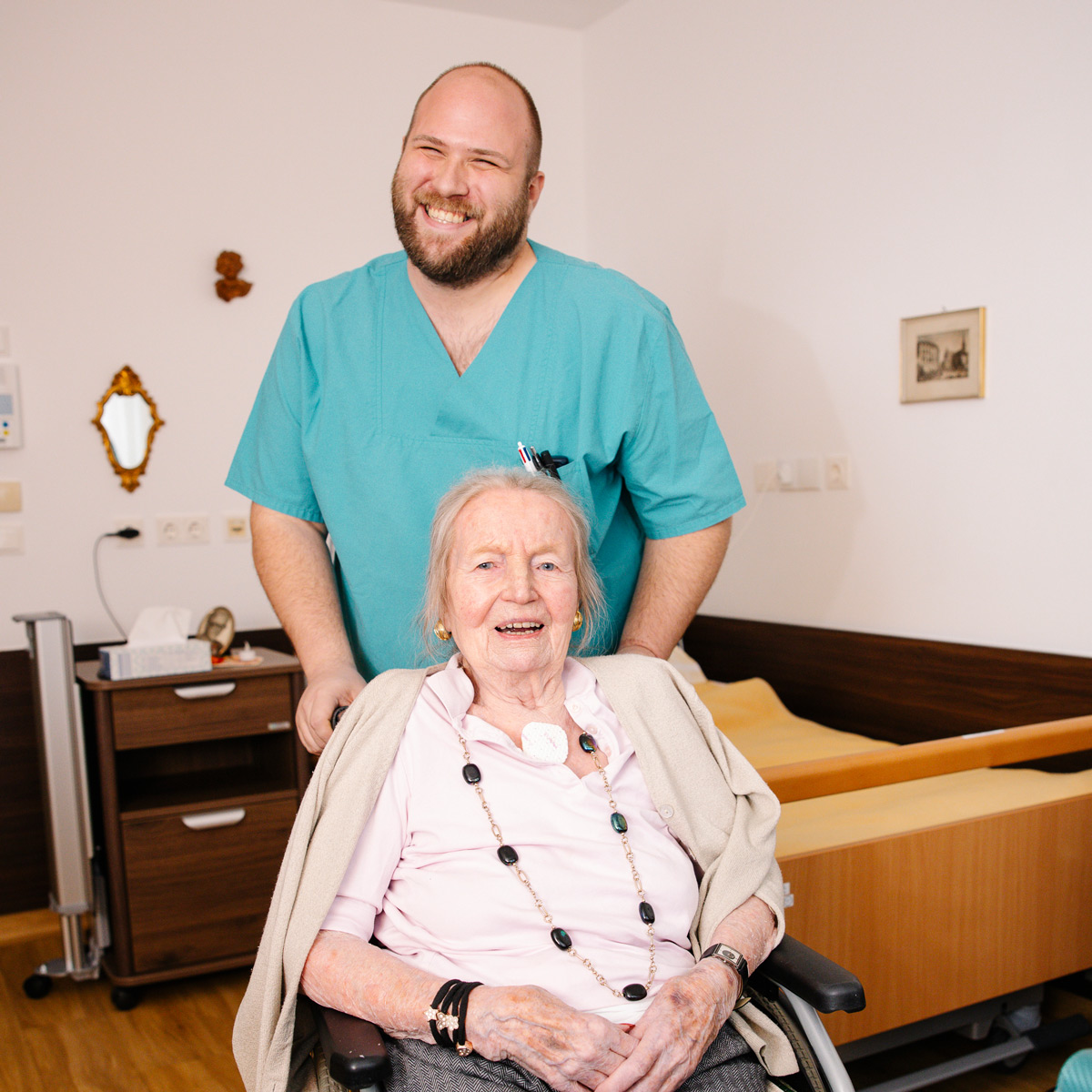 Ein Pfleger und eine Bewohnerin im Rollstuhl lächeln zufrieden