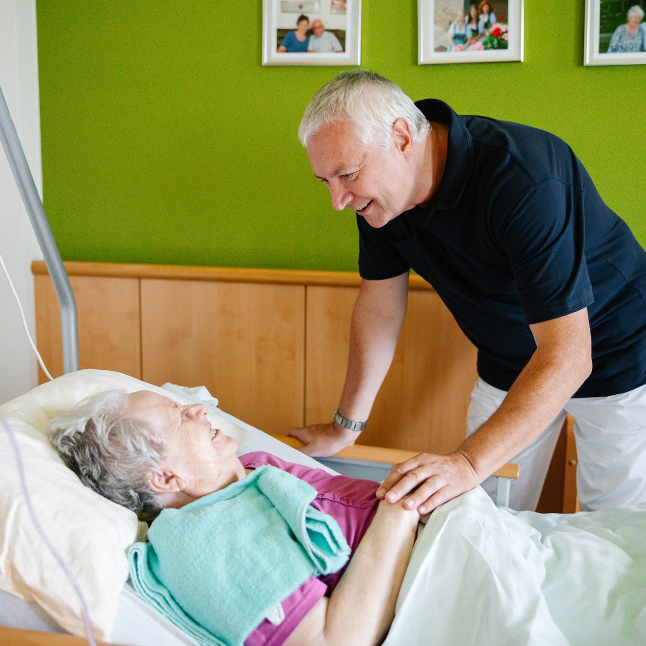 Ein Seelsorger hält liebevoll die Hand einer pflegebedürftigen älteren Dame im Pflegebett.
