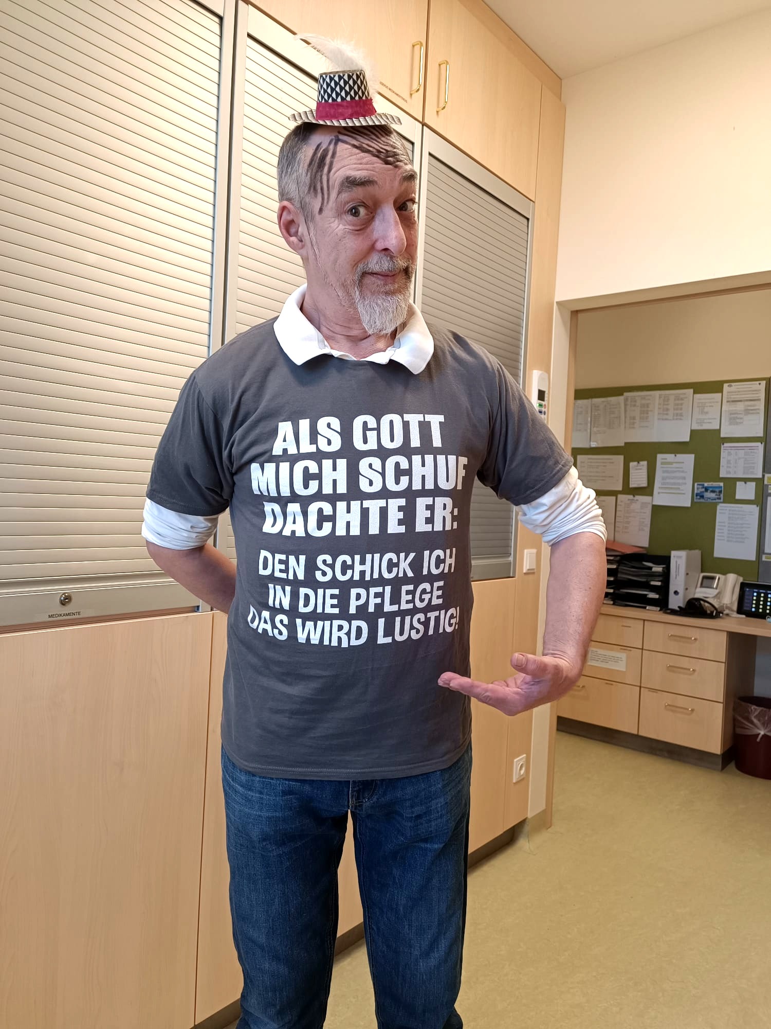 Ein Pfleger trägt zu Fasching ein T-Shirt mit der Aufschrift: "Als Gott mich schuf dachte er: Den schicke ich in die Pflege, das wird lustig."