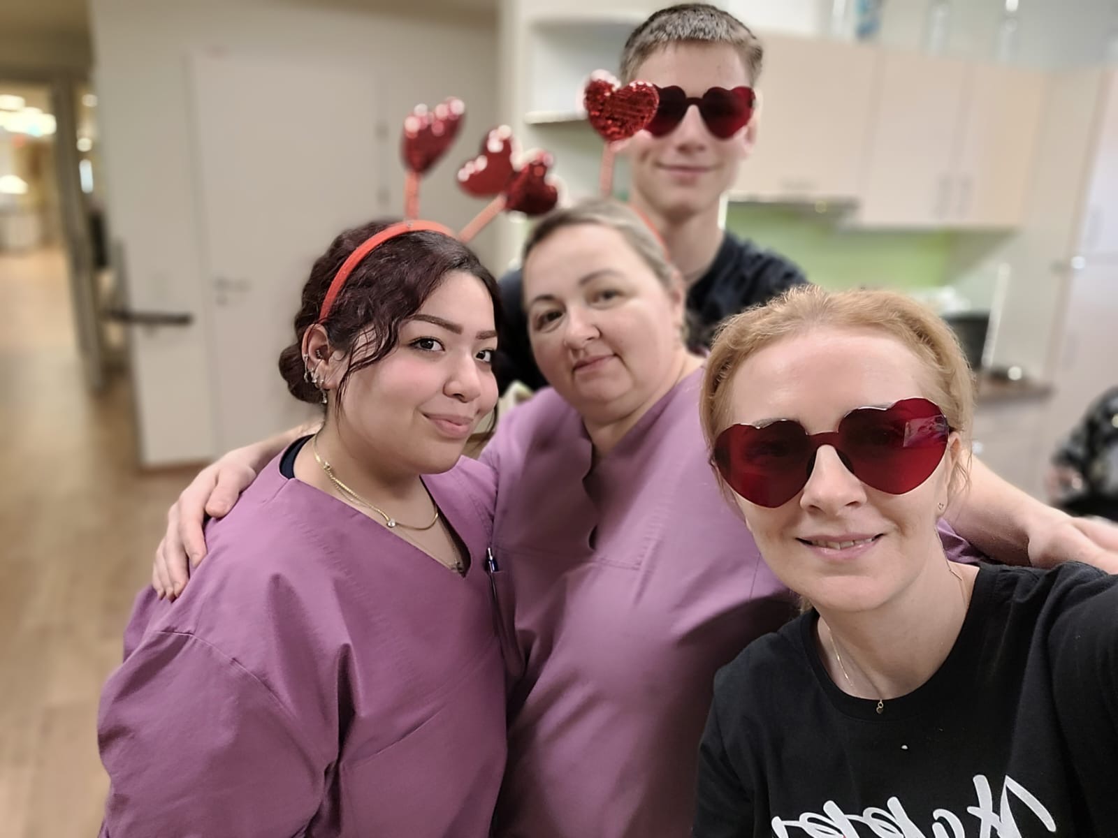 Vier Pflegekräfte posieren mit Herz-Sonnenbrillen und Kopfschmuck bei einem Selfie.