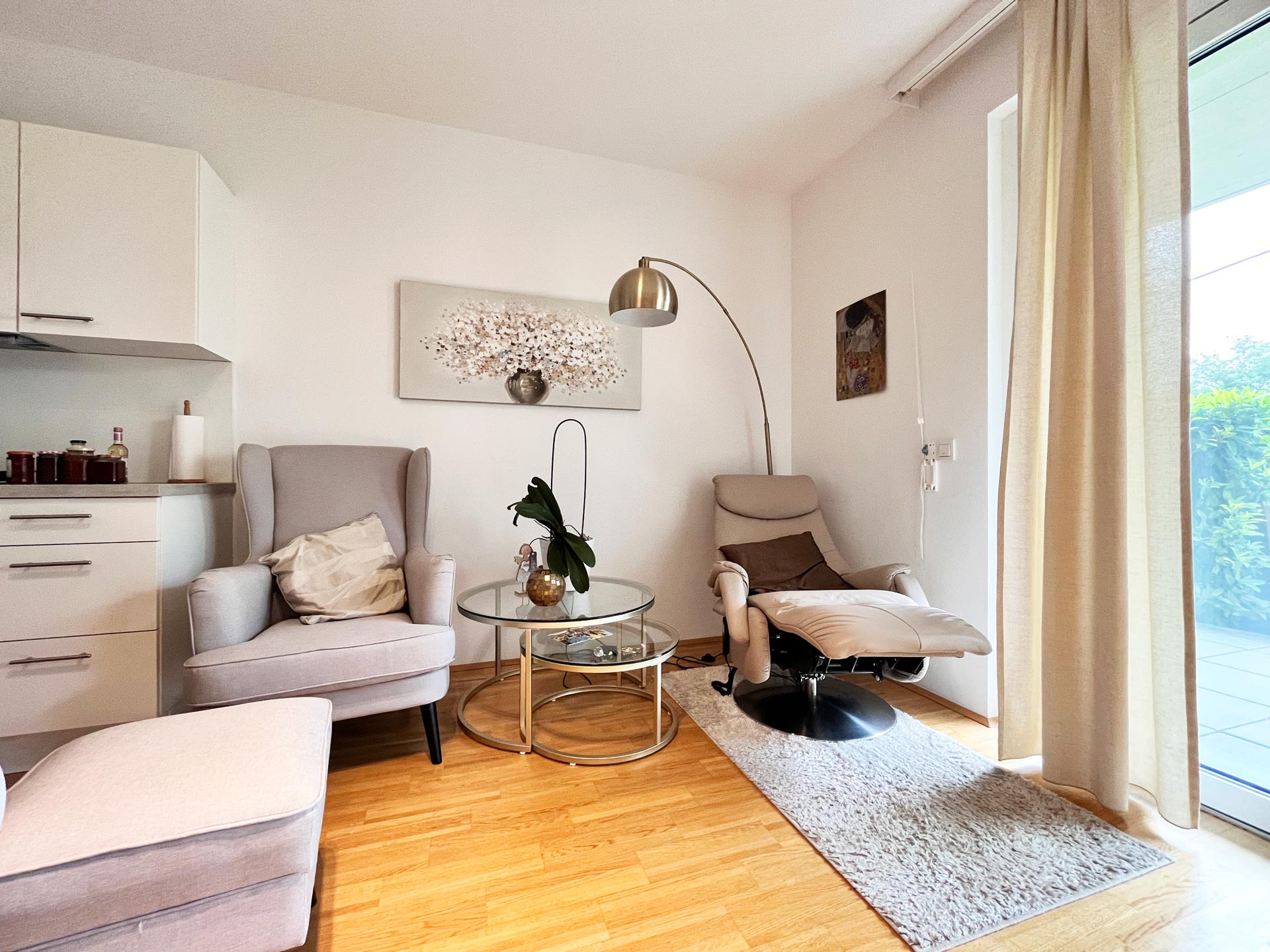Gemütliches Wohnzimmer mit Lehnsessel und Ausblick auf die Terasse mit Garten