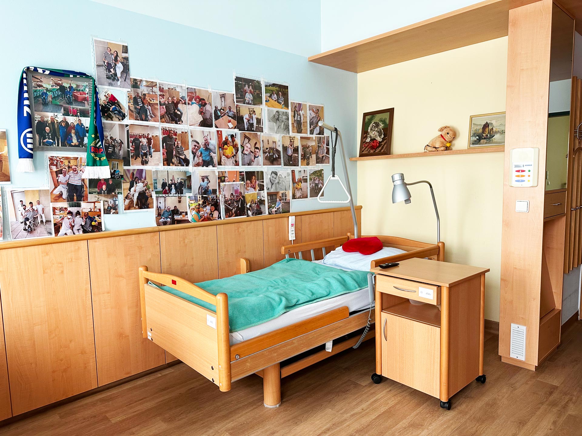 Gemütliches Pflegebett mit Nachttisch und vielen Erinnerungsfotos an der Wand