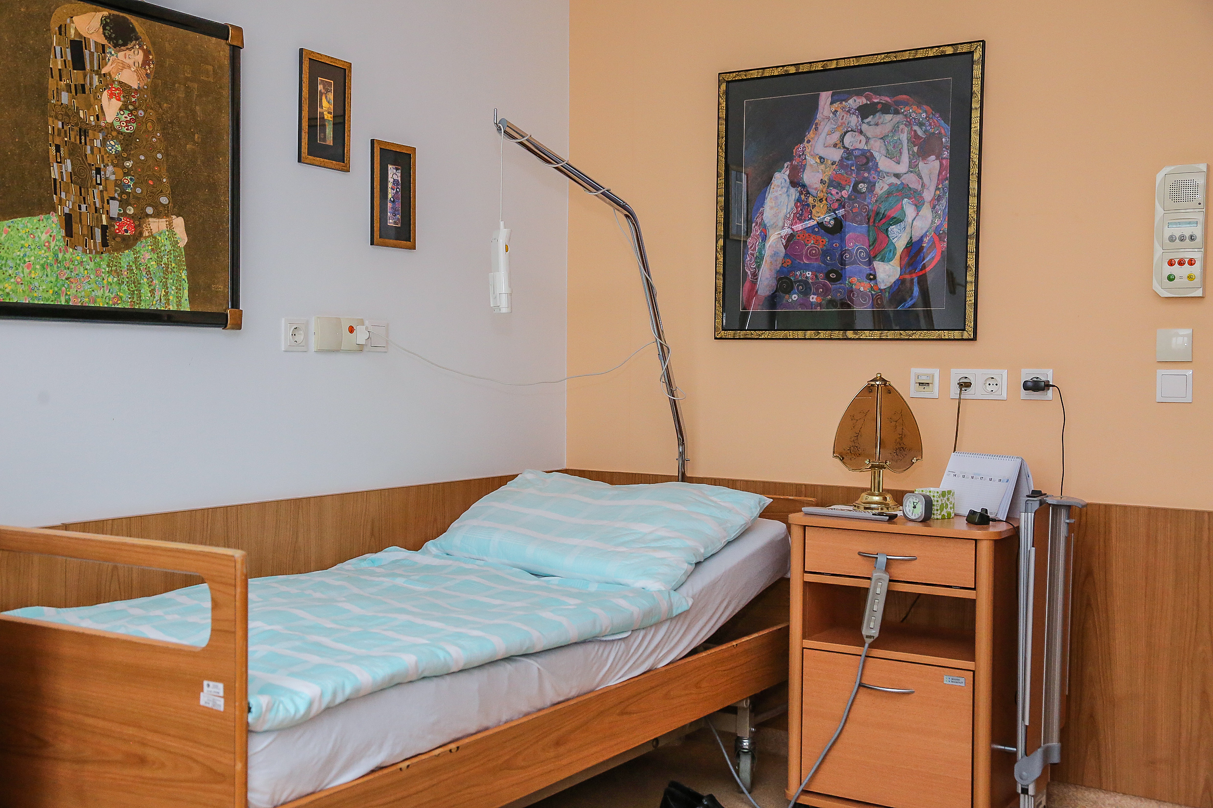 Ein Pflegebett mit persönlicher Einrichtung: Diverse Klimtbilder an der Schlafzimmerwand..