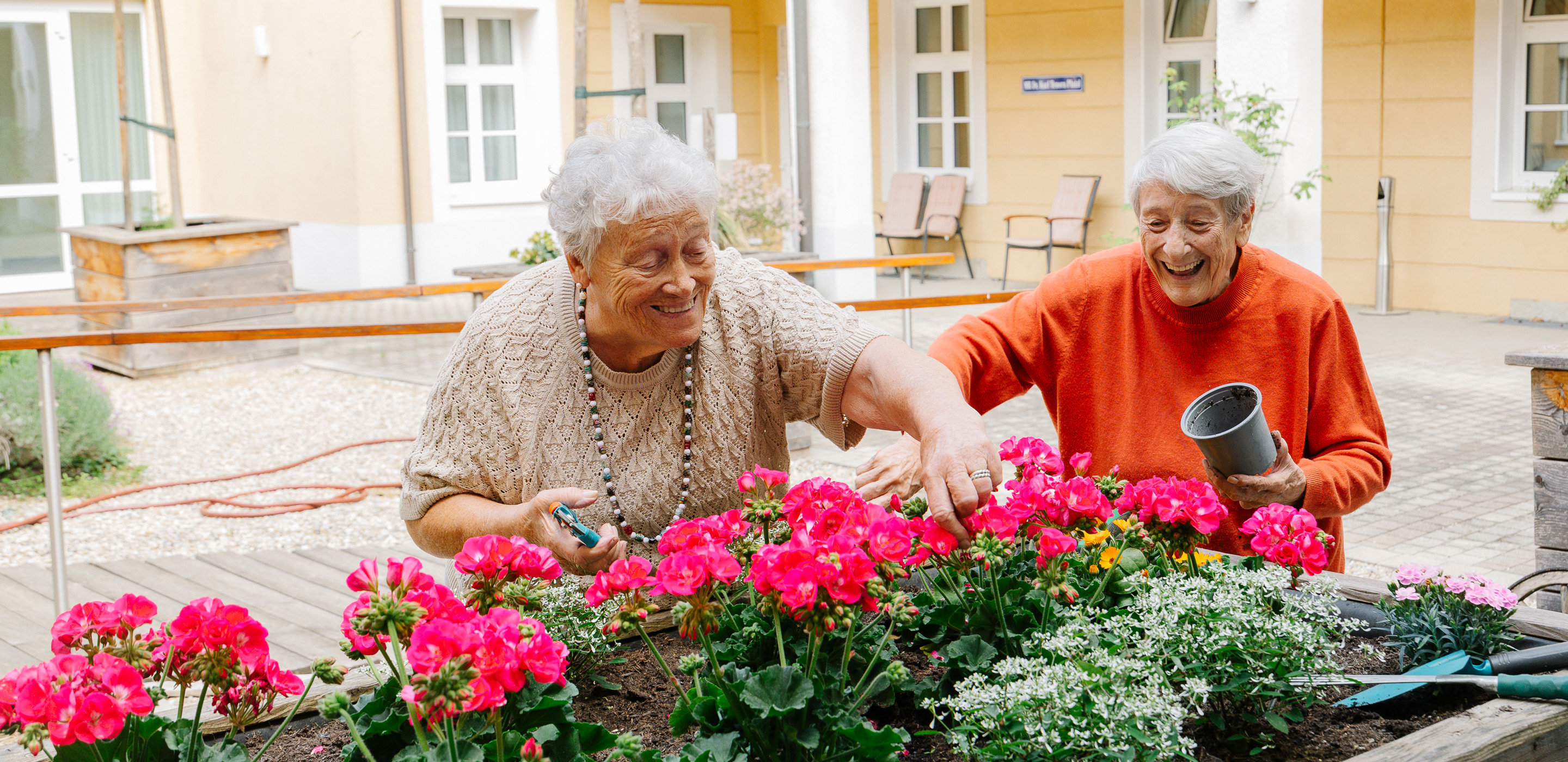 Zwei Bewohnerinnen setzen Blumen im Hochbeet ein
