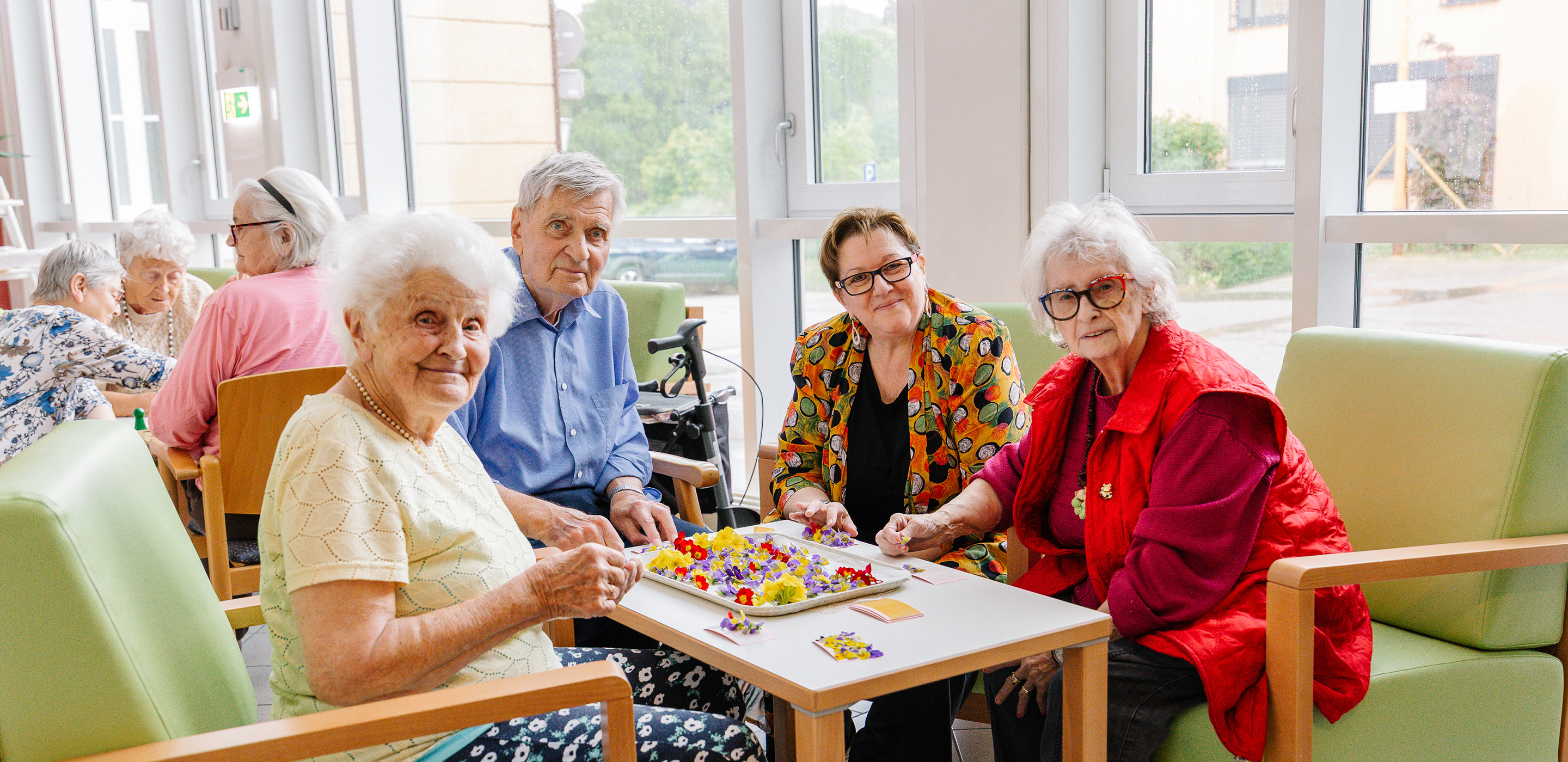 Einige Bewohner*innen und eine Ehrenamtliche sitzen zufrieden zusammen und basteln Blumengestecke