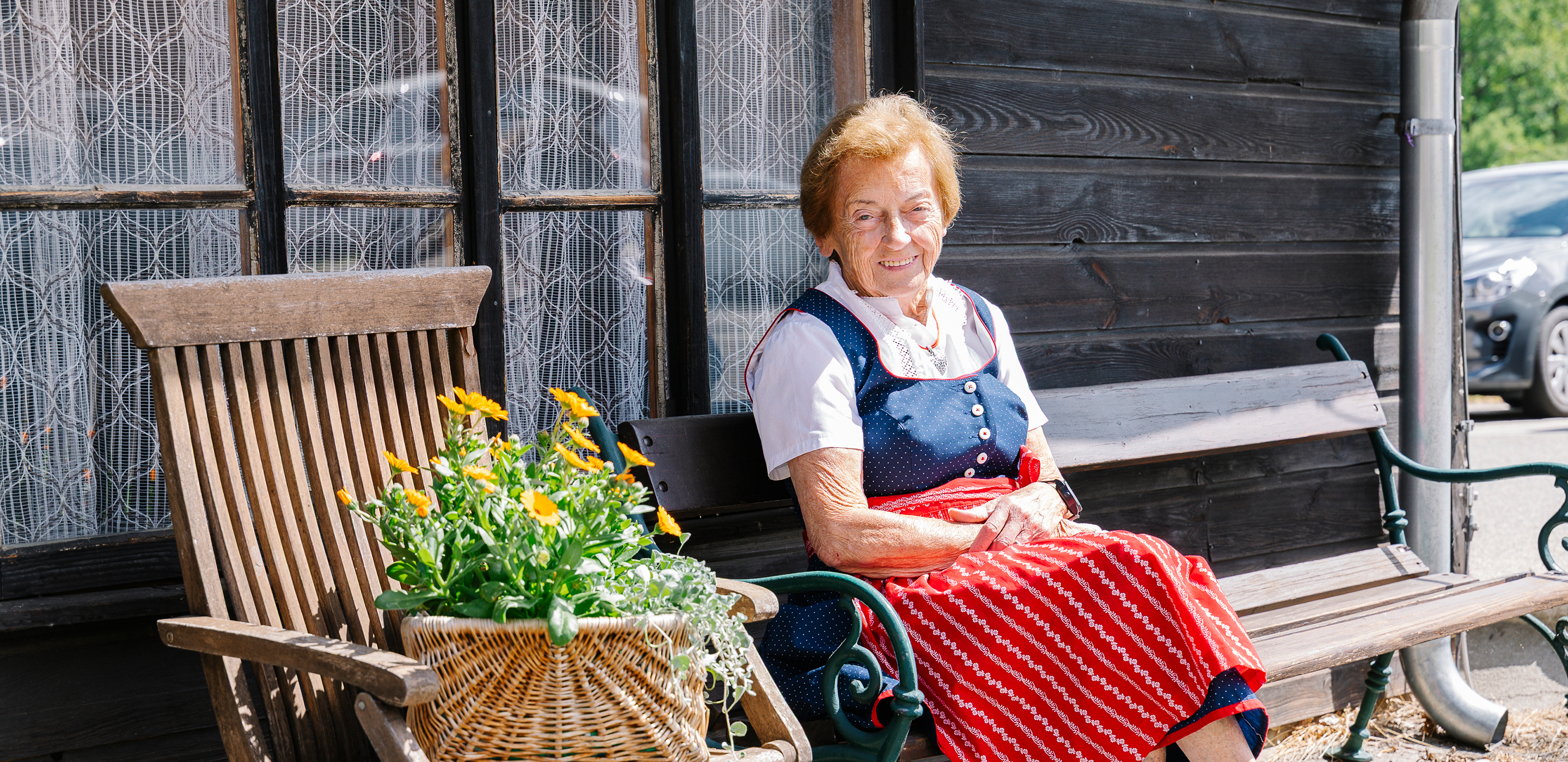 Eine Bewohnerin im Dirndl sitzt vor Blumen im Garten