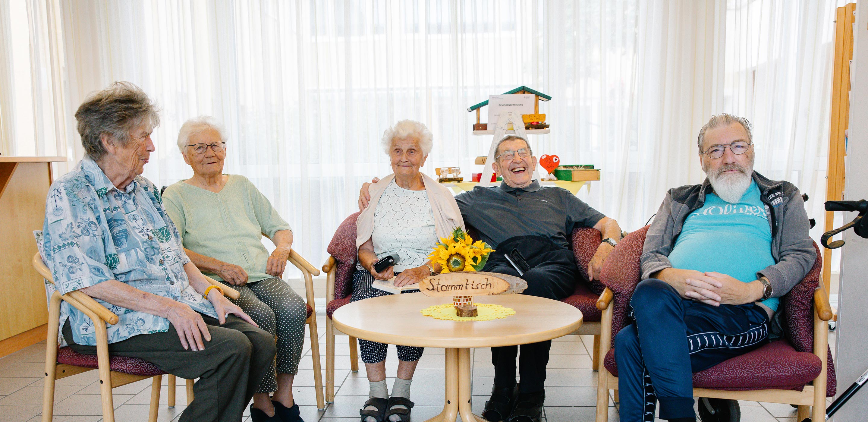 Bewohnerinnen und Bewohner im Pflegehaus sitzen gemütlich am Stammtisch