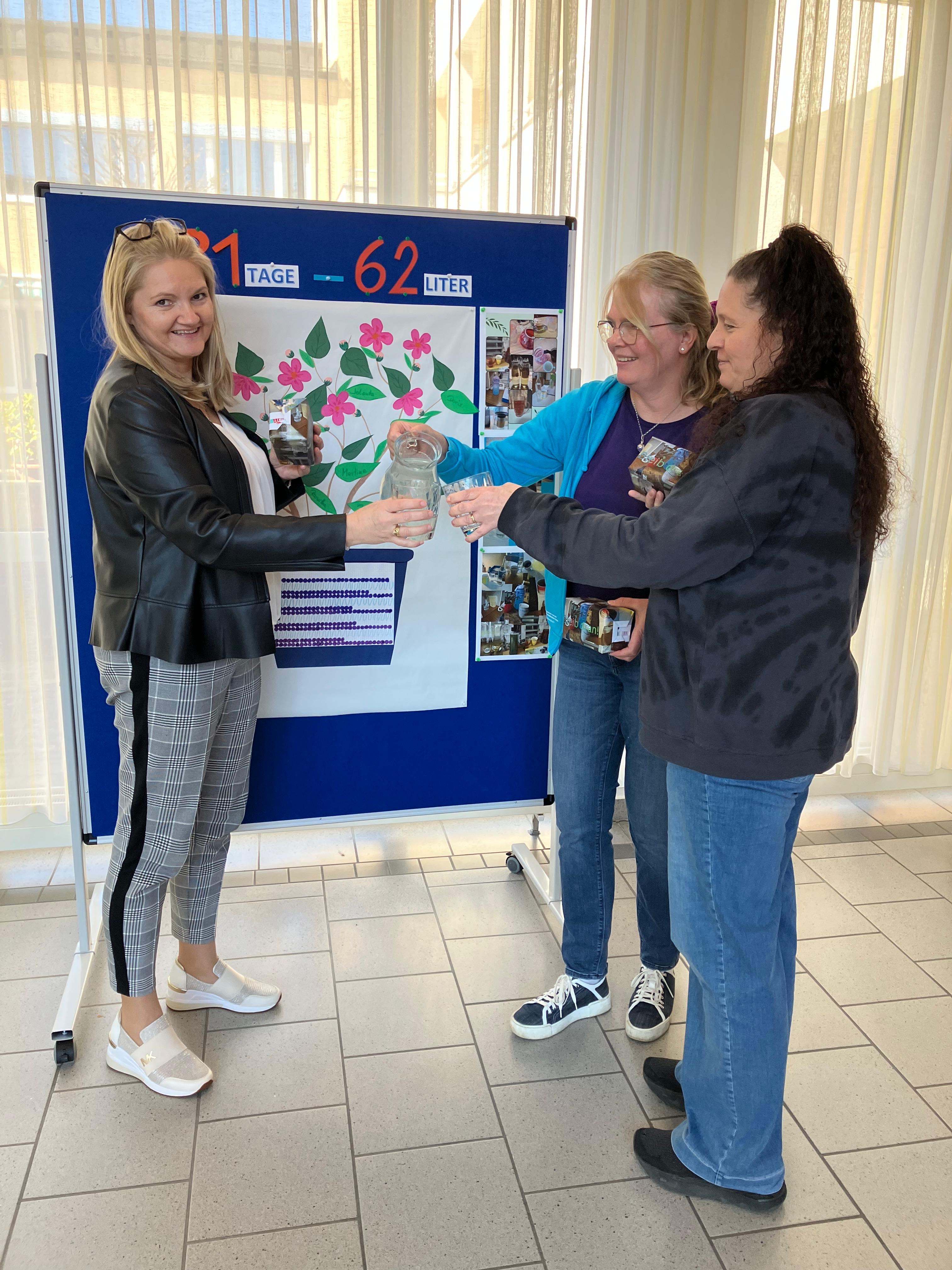 Drei Mitarbeiterinnen stoßen gemeinsam mit einem Glas Wasser an.