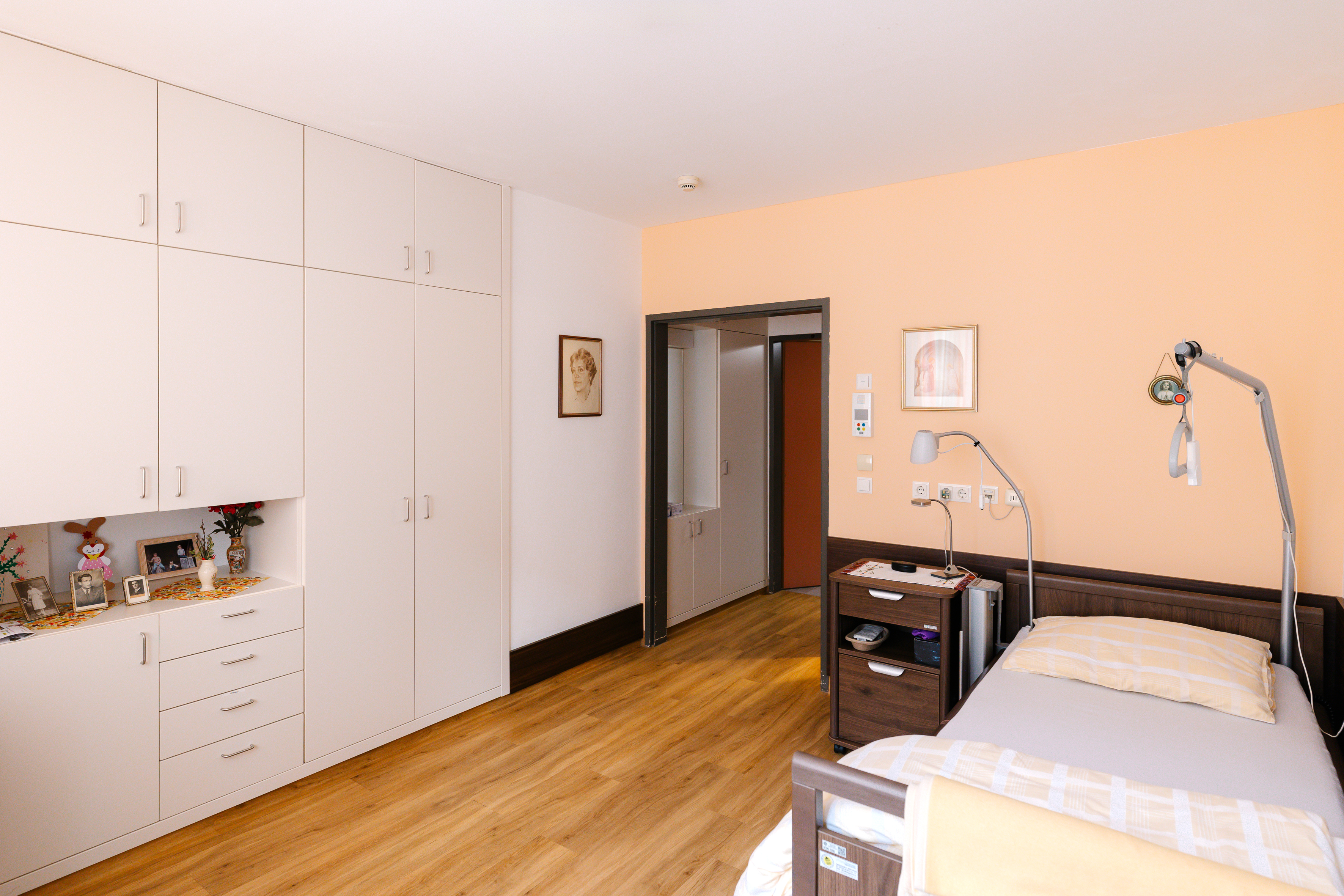 Ein modern eingerichtetes Zimmer im Pflegehaus mit Einbauschrank, Pflegebett und Parkettboden.